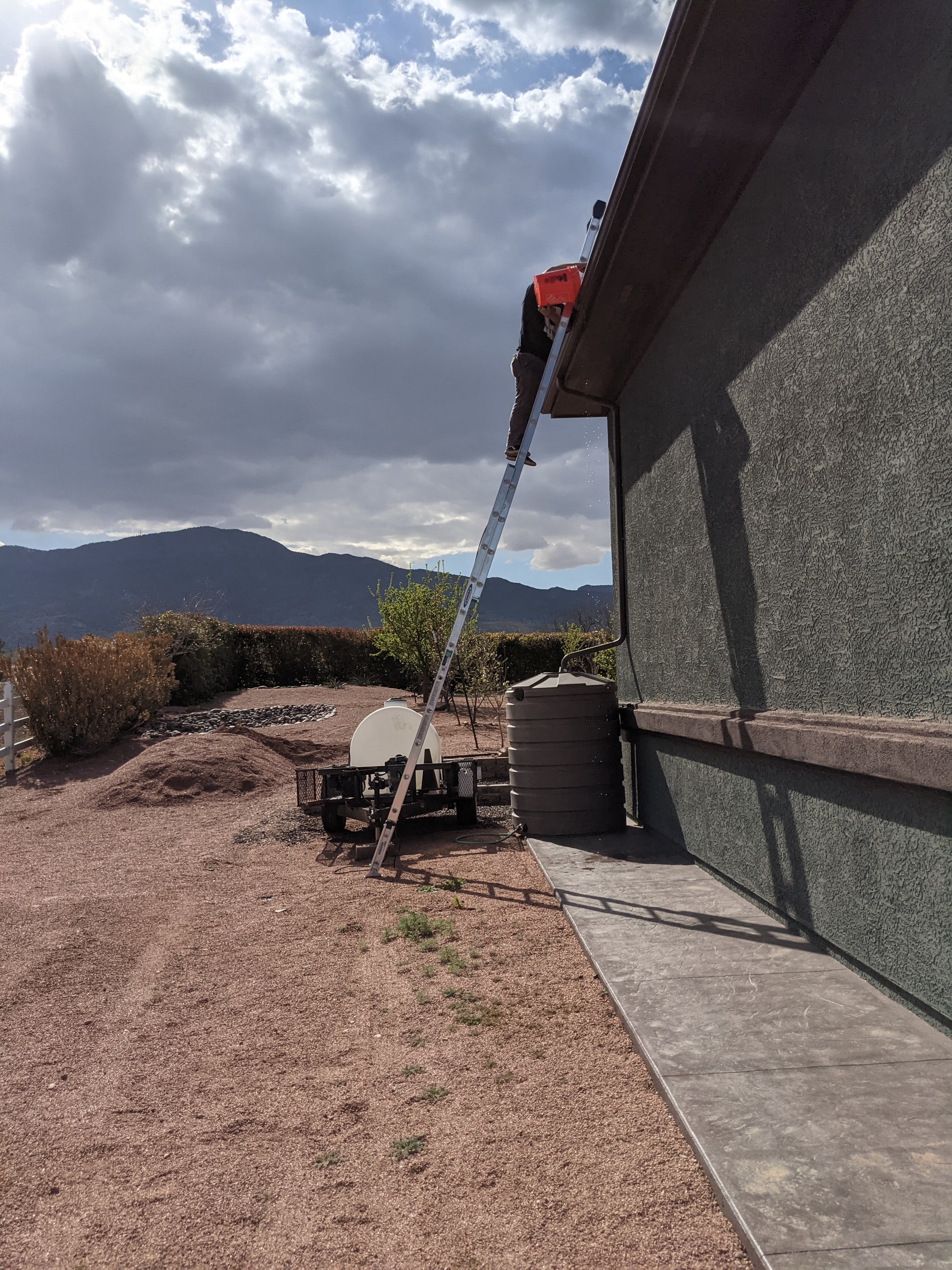 Gutter cleaning on a roofline in Cottonwood, AZ with Verde Valley landscape and clouds in background