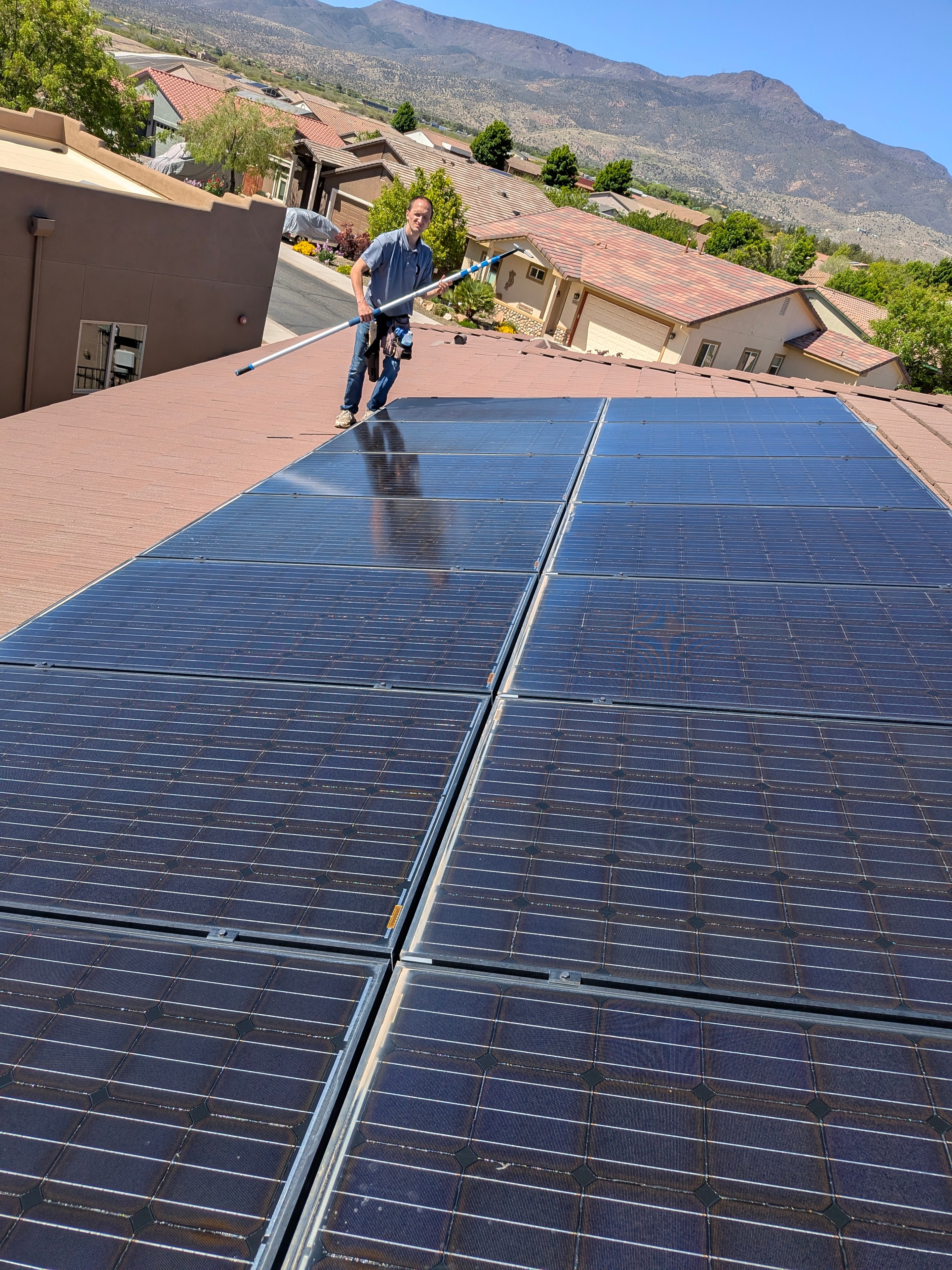 Demigod technician cleaning solar panels on a tile roof in Cottonwood with Verde Valley mountains in background