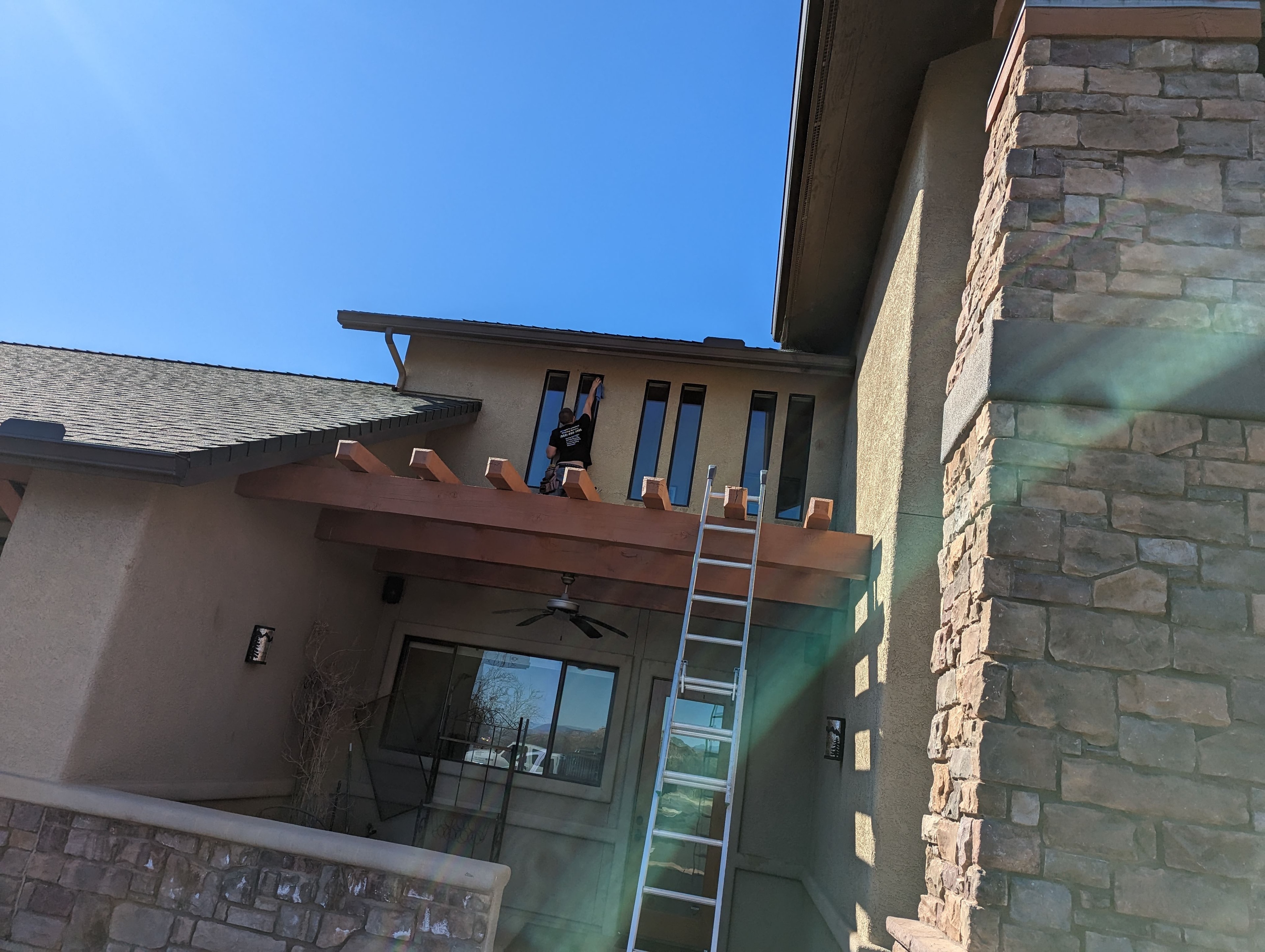 Window cleaner on ladder cleaning high windows on a stucco home with pergola in Cottonwood, AZ
