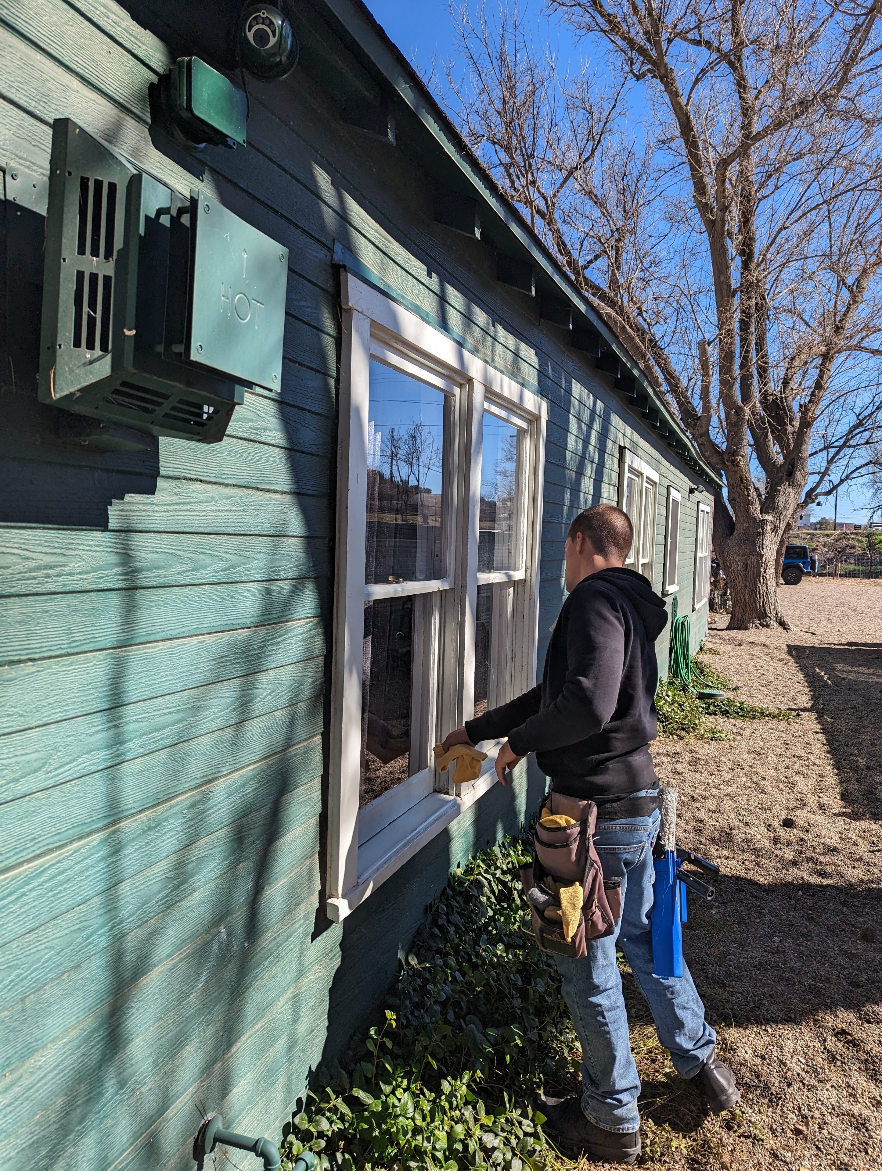Demigod technician cleaning windows on a teal wood-sided residential home in Cottonwood, Arizona
