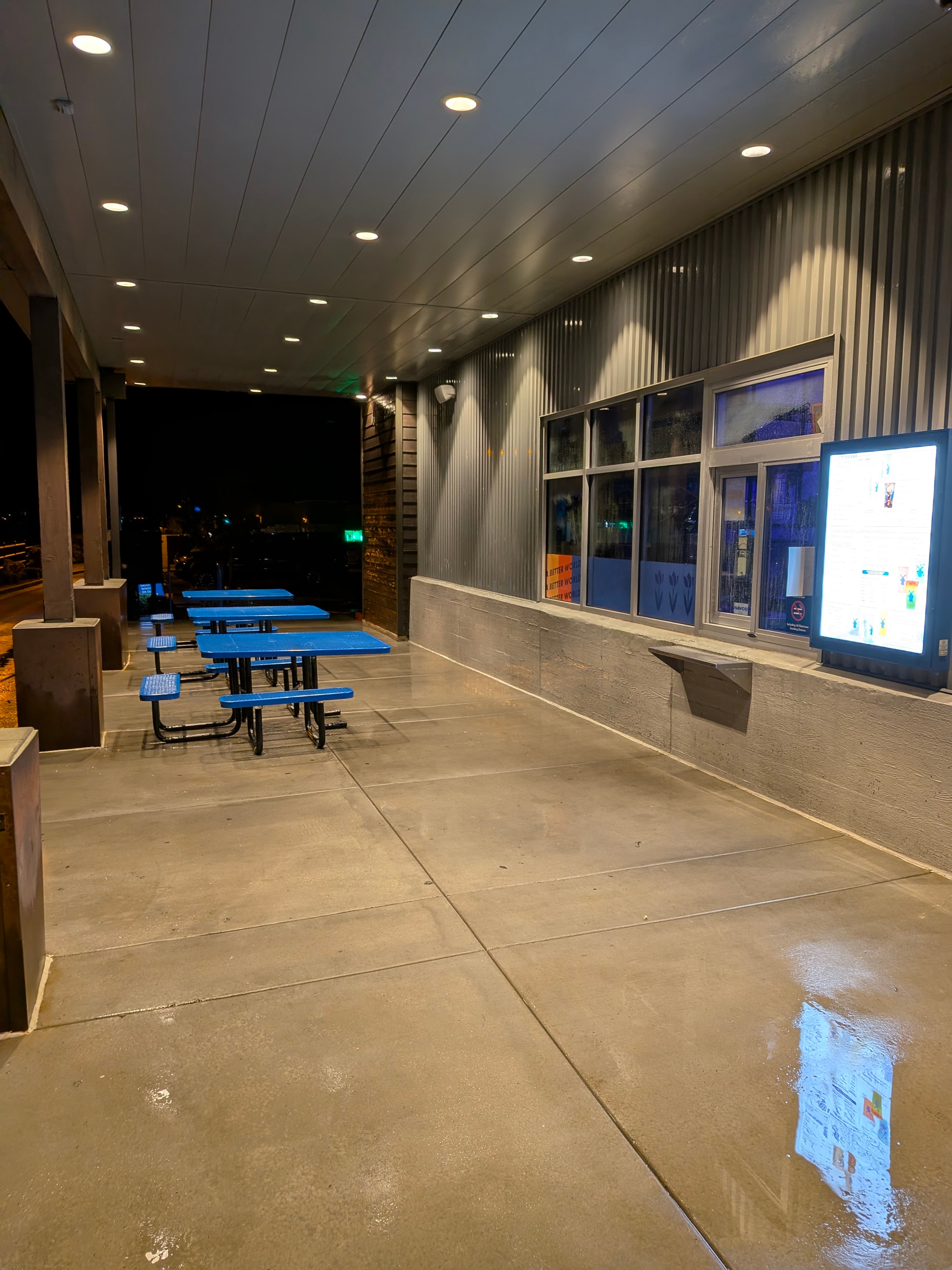 Freshly pressure washed commercial patio and concrete at a Flagstaff business at night — gleaming clean with blue picnic tables and modern corrugated metal exterior