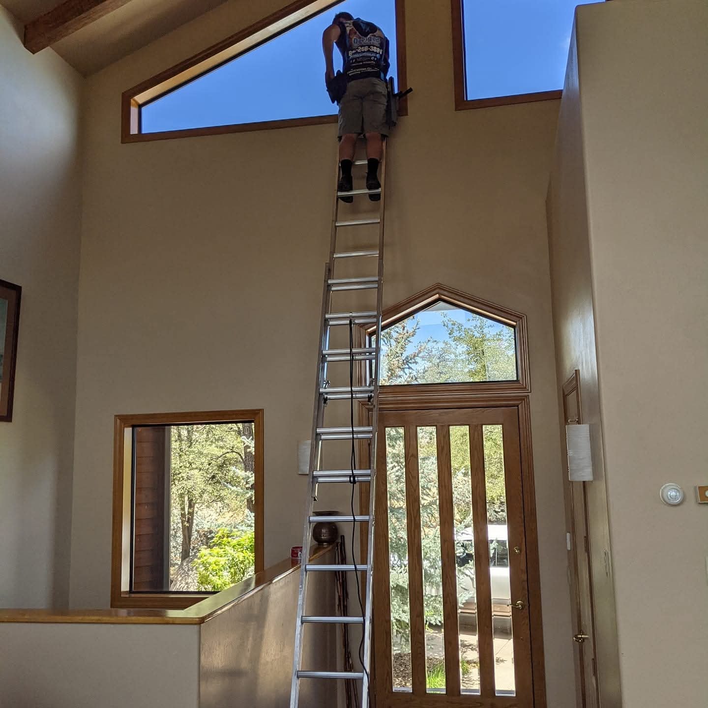 Demigod technician on tall extension ladder cleaning high interior windows at a Flagstaff adobe home with vaulted ceilings