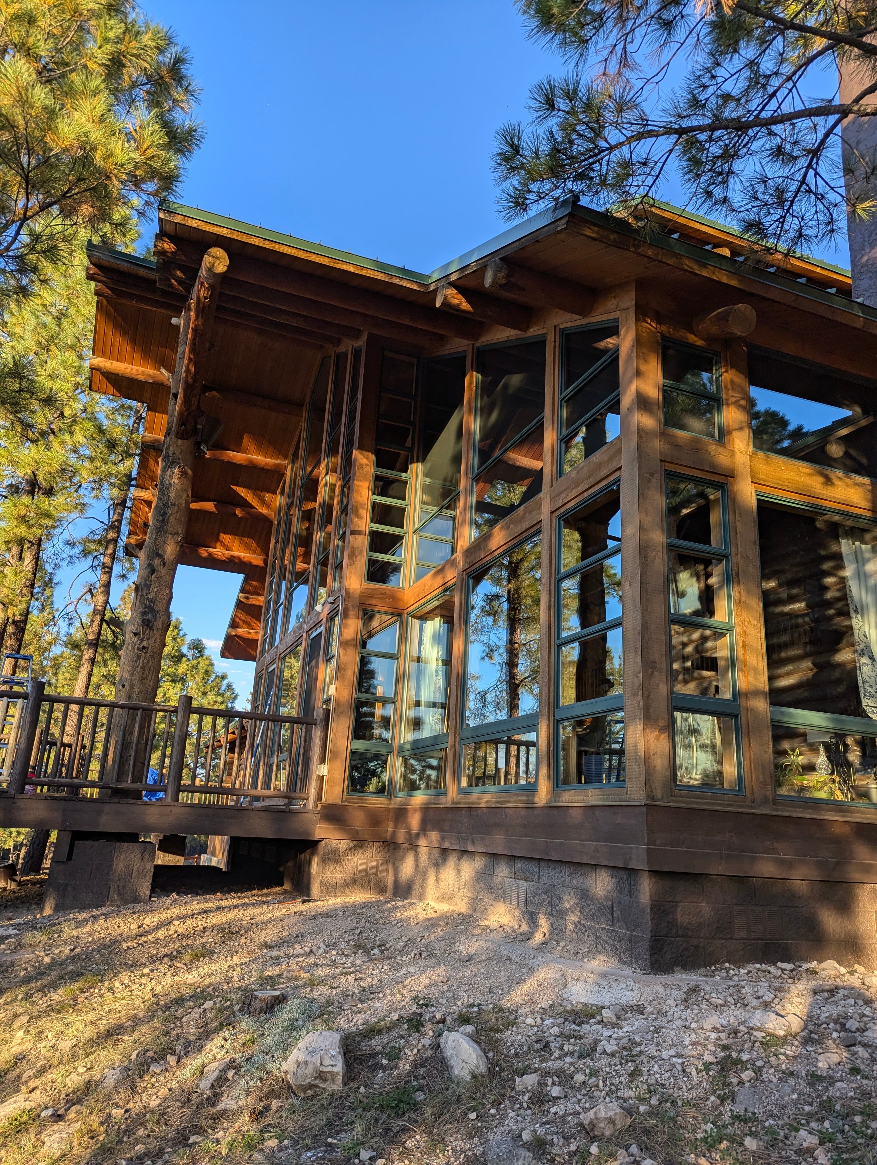 Log cabin exterior in Flagstaff, AZ with floor-to-ceiling clean windows reflecting ponderosa pines in golden hour light