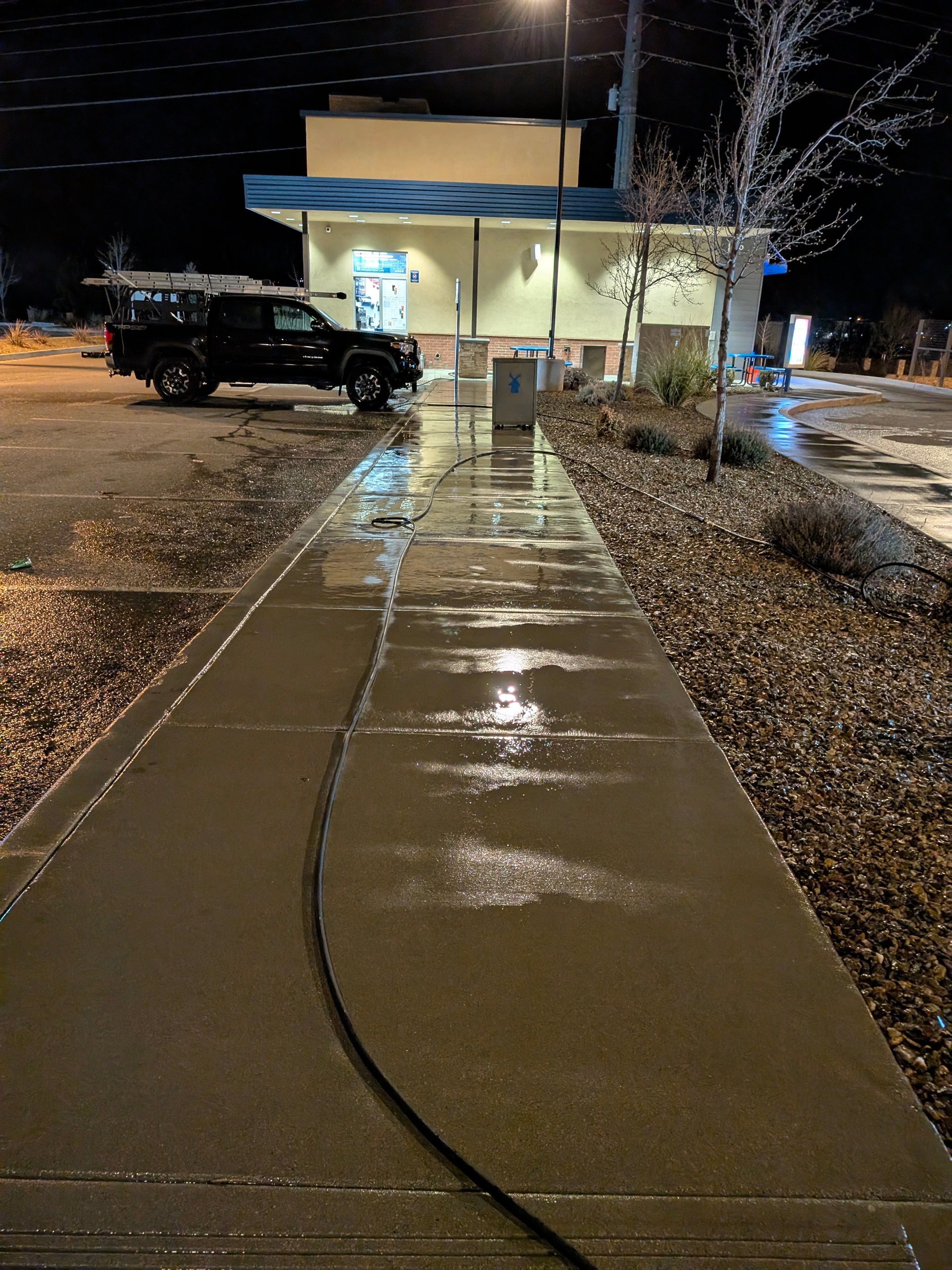 Freshly pressure washed concrete sidewalk at Dutch Bros Coffee in Prescott, AZ — gleaming clean at night with Demigod truck visible