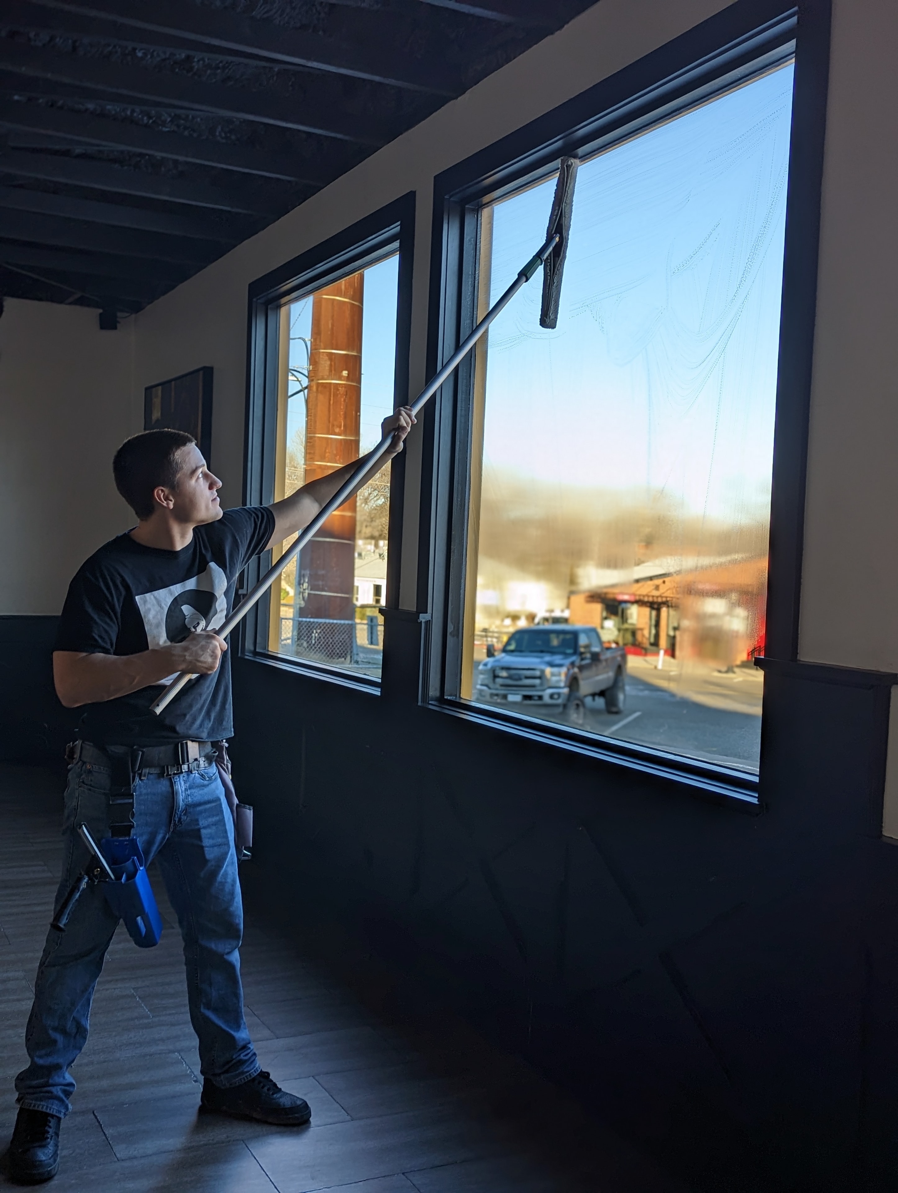 Demigod technician using extension pole to clean large interior commercial windows at a Prescott business