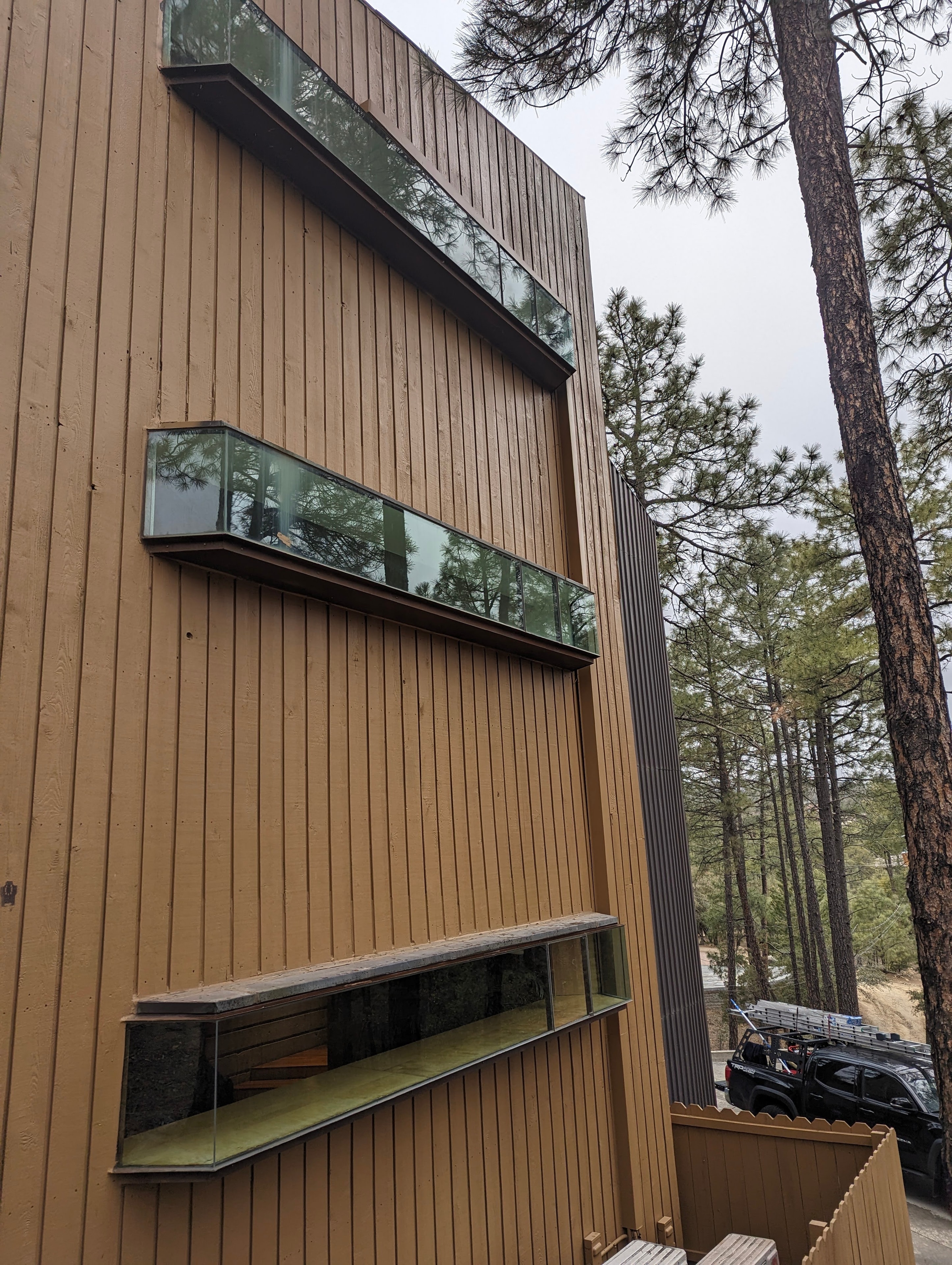 Clean floor-to-ceiling windows on a modern vertical-siding cabin in Prescott, AZ surrounded by ponderosa pine trees