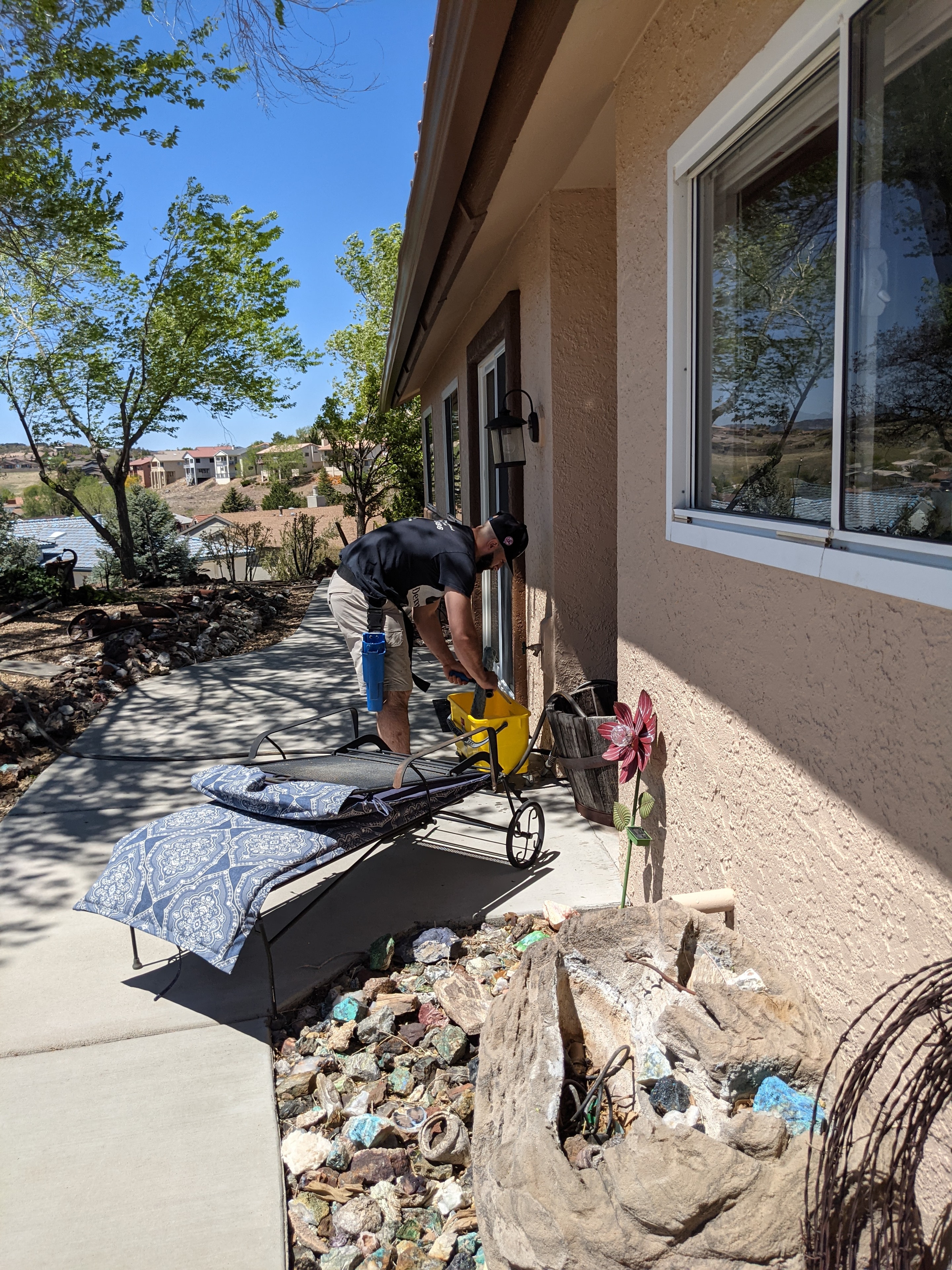 Demigod technician cleaning window frames and sills on a stucco home in Prescott, AZ with desert rock landscaping
