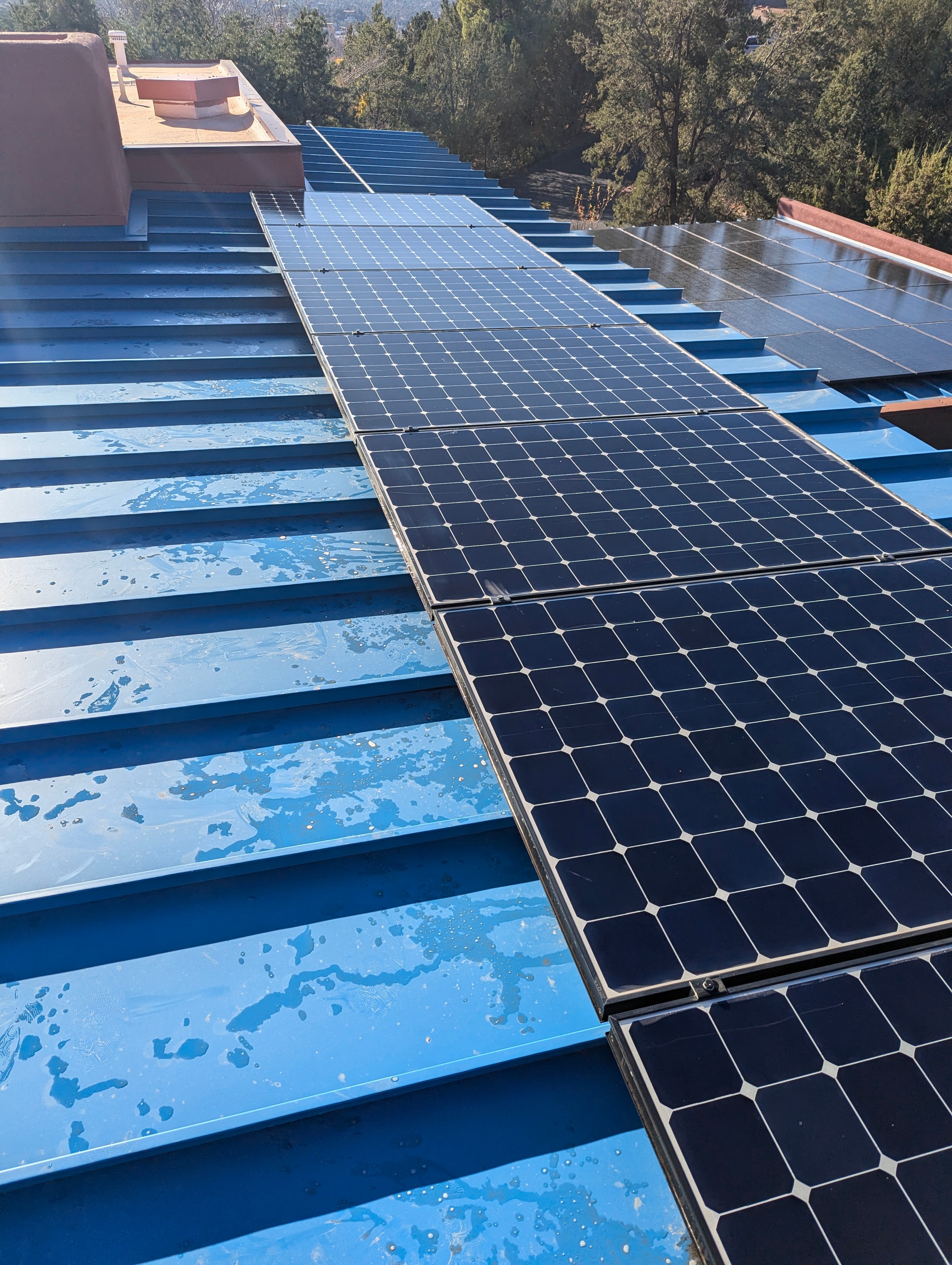 Solar panels being cleaned on a blue metal roof in Sedona, Arizona