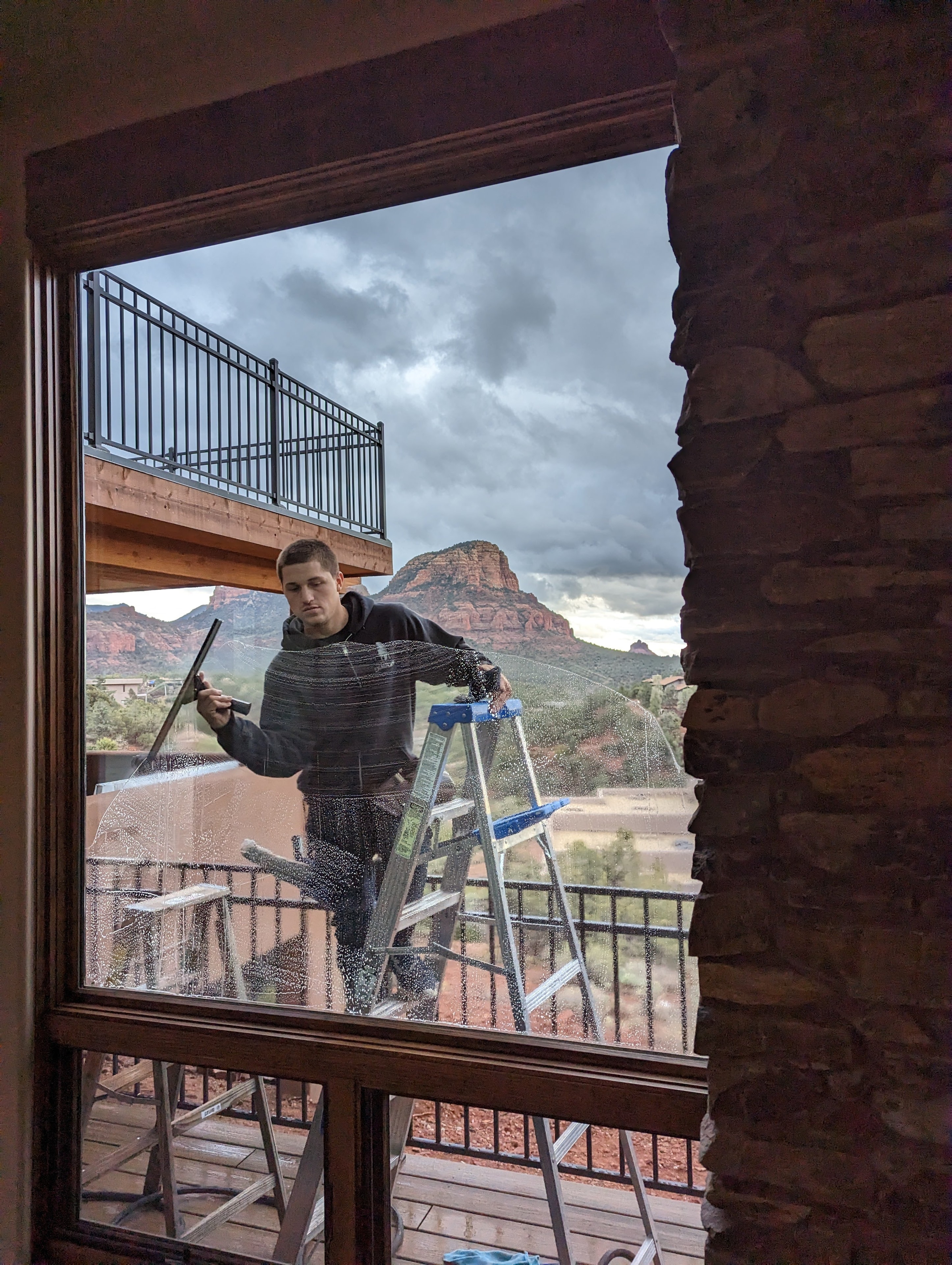 Window cleaner on ladder cleaning windows of a Sedona home with red rock formations in the background