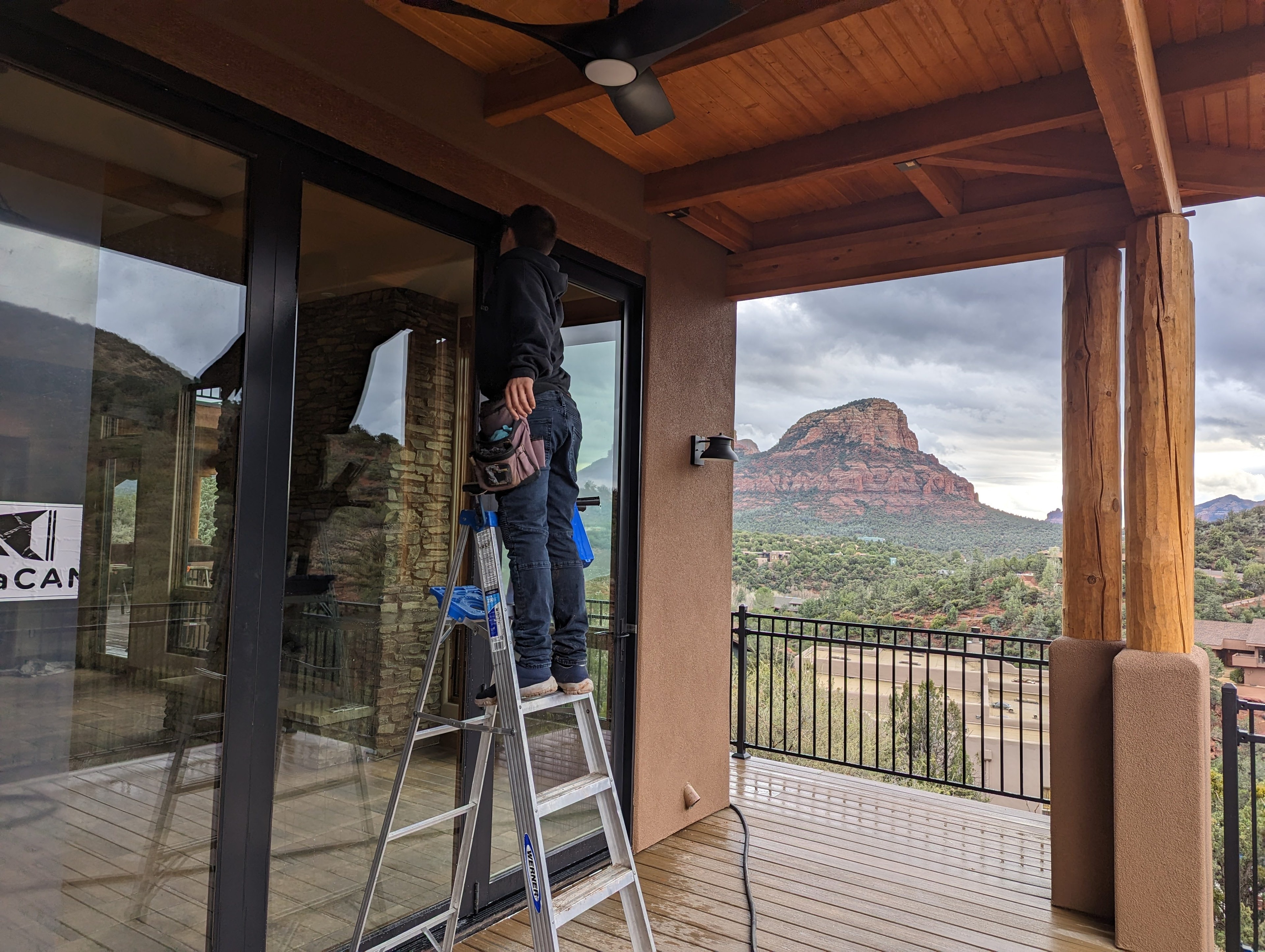 Window cleaner on ladder cleaning sliding glass door at a Sedona property with Bell Rock visible in background